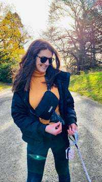 Thumbnail for Woman with dark hair wearing a TopDog Harnesses Everyday Essential dog walking bag in the park on a sunny day
