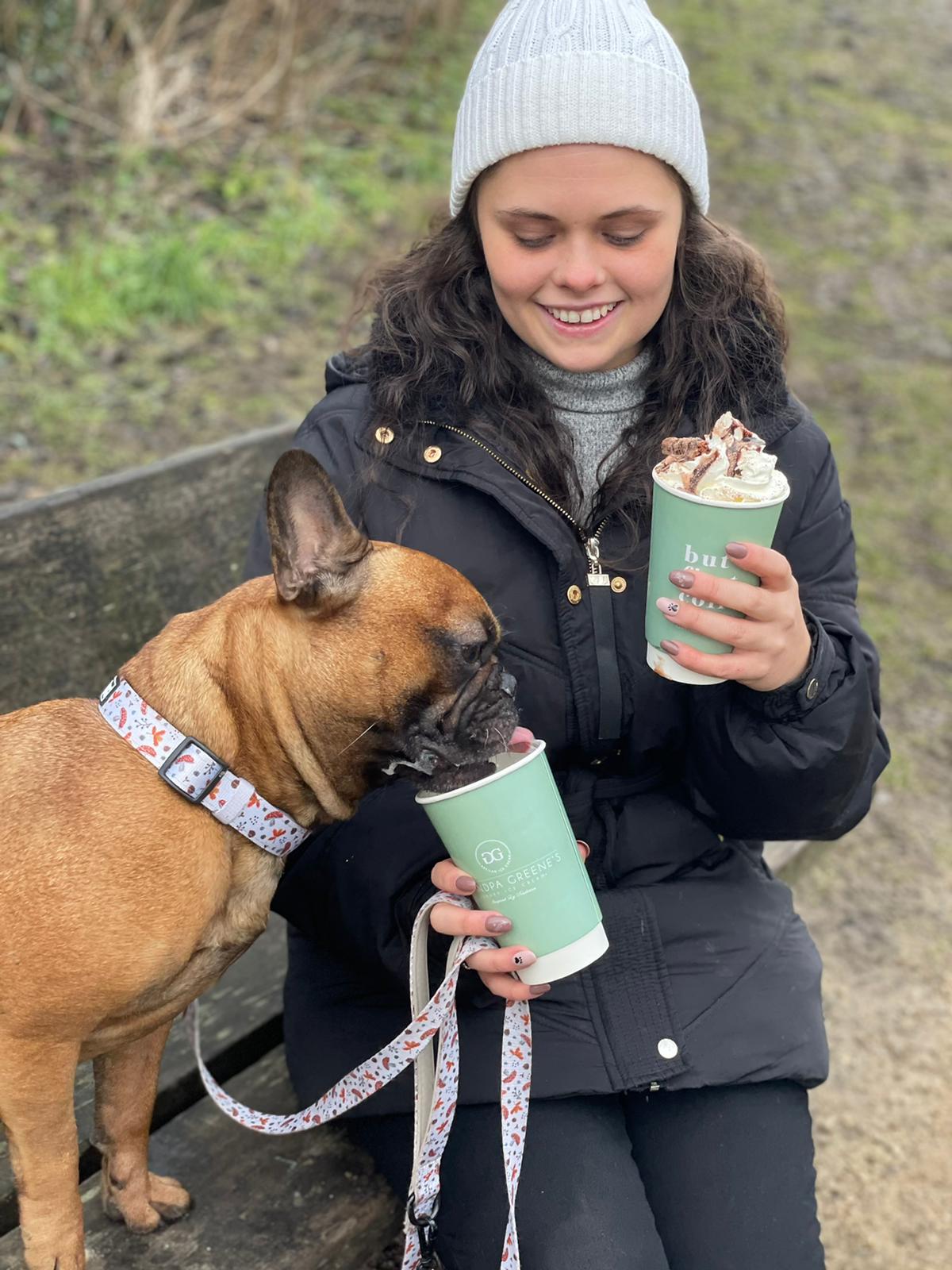 French bulldog wearing TopDog Harnesses Woodland Treasures Dog Collar, sitting on a bench with young woman owner both drinking winter drinks
